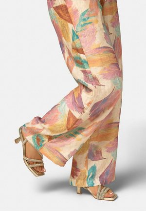 Pantalones fluidos con patrones abstractos de hojas en tonos pasteles, combinados con sandalias de tacón de punta cuadrada que cuentan con tiras cruzadas brillantes.