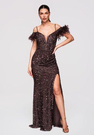 Kvinde i en mørkelilla palietteret skulderfri kjole med fjerærmer og slids op til låret, iført guld høje hæle sandaler.