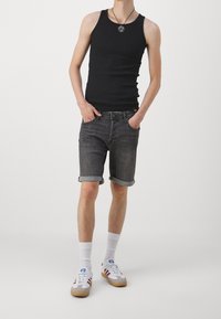 Černý tílko, tmavě šedé džíny s ohrnutým lemem, bílé sportovní ponožky a tenisky s červenými a modrými akcenty, minimalistický design.