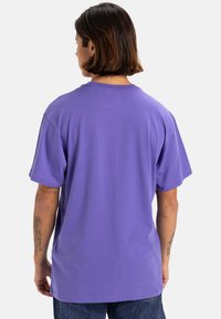 Camiseta de algodón morada con un corte relajado, mangas cortas y cuello redondo, que presenta una textura suave y un ligero estiramiento.