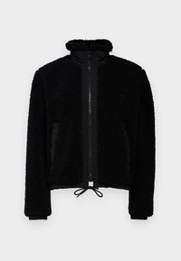 Czarna polarowa kurtka z wysokim kołnierzem, zamek błyskawiczny z przodu i elastycznym sznurkiem w dolnej części. Gładkie panele boczne i teksturowana część główna dla większego ciepła.