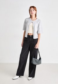 Grå strikket kortermet cardigan, kremfarget cropped topp, svarte vide jeans, hvite spisse ankelstøvletter og en teksturert blå håndveske.