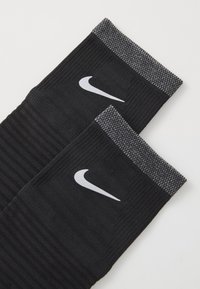 Chaussettes de sport noires avec une texture côtelée et des accents gris en haut. Présentent le logo swoosh blanc de Nike sur chaque chaussette.