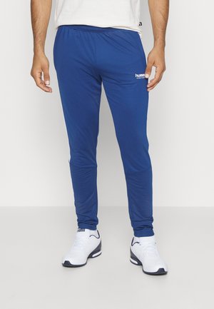 Blauwe sportbroek van rekbaar materiaal met een elastische tailleband. Beschikt over een wit logo op de bovenbeen en een taps toelopend ontwerp bij de enkels.