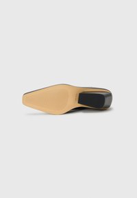 Suola di scarpa nera con un design semplice, caratterizzata da una base in gomma color cuoio con una leggera tacca. Sono visibili linee scanalate per la trazione.