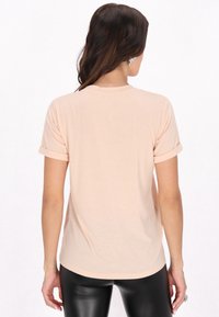 Lyserød kortærmet T-shirt med opfoldede ærmer, rund halsudskæring og en glat stoftekstur. Løs pasform, subtil buet kant forneden.