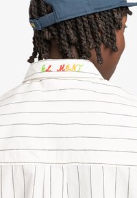 Witte shirt met zwarte verticale strepen en kleurrijke "ELEMENT" borduursel op de kraag. Het materiaal lijkt lichtgewicht met een gladde textuur.