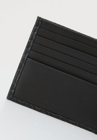 Portafoglio in pelle nera con più slot orizzontali per carte, dettagli texture sui bordi e un logo discreto in basso.