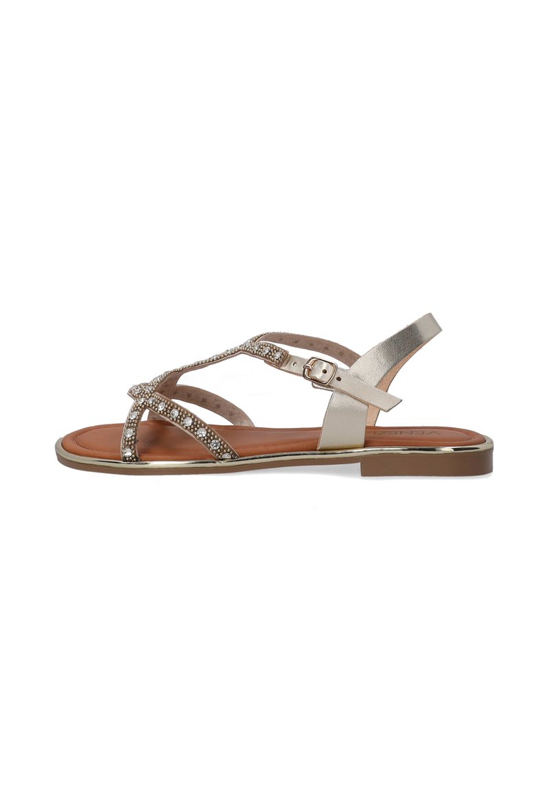 Metallisch goldene Sandalen mit überkreuzten Riemen und Strassakzenten. Flache Sohle mit Schnallenverschluss und braunem Fußbett. Mid-Heel-Design.