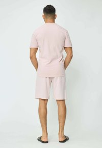 T-shirt en coton rose clair et short assorti, manches courtes, coupe décontractée, design uni ; porté avec des tongs noires, vu de dos.