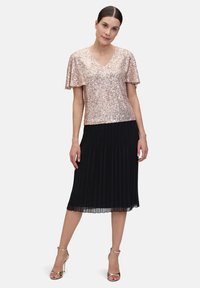 Pailletten top in rosegoud met een V-hals en korte mouwen, gecombineerd met een zwarte geplooide midi rok. Gouden enkelbandjes op de hakken maken de look compleet.