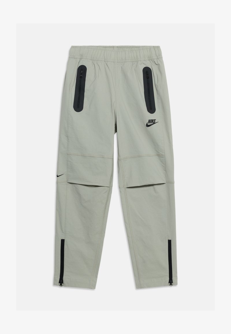 Ανοιχτό γκρι παντελόνι Nike με ελαστική μέση, μαύρες τσέπες με φερμουάρ στους μηρούς, επιθέματα στα γόνατα και φερμουάρ στους αστραγάλους. Μαύρα λογότυπα Nike στους μηρούς και στις γάμπες.