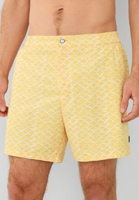 Žuti kupaći šortsi s bijelim valovitim uzorkom, elastični struk, zatvaranje na gumb i bočna džep za praktičnost.