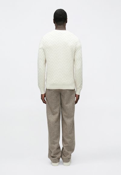 Pull en maille beige clair avec un motif texturé, associé à un pantalon ample marron clair. L'ensemble présente des poignets et un ourlet côtelés.