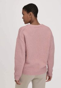 Rosa Strickpullover mit geripptem Saum und Bündchen, mit lockerer Passform und Raglanärmeln. Die Textur wirkt weich und leicht flauschig.