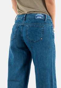 Vaqueros de denim azul con un corte relajado, con dos bolsillos traseros y una etiqueta en la cinturilla con un patrón azul. Textura suave con un ligero desvanecimiento.