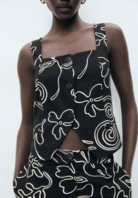 Svart och vit blommönstrad crop top med fyrkantig halsringning, stora knappar och en unik asymmetrisk design. Lättviktig tyg.