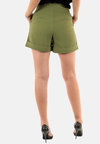 Shorts verts texturés avec un ourlet replié, des poches latérales et une taille ajustée. Associés à des chaussures à talons noirs.