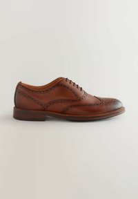 Pantofii de bărbați din piele maro, tip brogue, cu perforații detaliate și vârful întunecat, pe un fundal neutru deschis.
