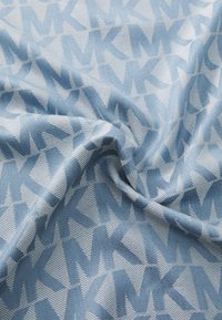 Tissu bleu clair présentant un motif texturé de lettres "MK" se chevauchant en tons de bleu plus foncé. Surface lisse avec un léger éclat.