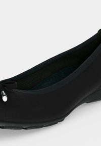Chaussure ballerine noire avec un petit nœud et des embouts métalliques argentés à l'avant, semelle texturée et semelle intérieure rembourrée.