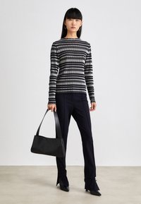 Gestreifter Schal mit Schwarz- und Weißstreifen aus Strick, kombiniert mit maßgeschneiderten schwarzen Hosen und einer schwarzen Handtasche mit einer glatten, matten Oberfläche.