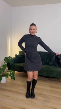 Temno siva obleka z dolgimi rokavi in visokim izrezom, s rahlo razširjeno krilom. Kombinirana s črnimi škornji do kolen in črno torbico v roki.