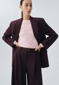 Maroon blazer with structured lapels, paired with a light pink sweater and matching high-waisted trousers, featuring pleats and a tailored fit.