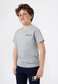 Szara bawełniana koszulka z okrągłym dekoltem, krótkimi rękawami i czarnym logotypem "Champion", zestawiona z ciemnymi spodniami i białym akcentem logo.