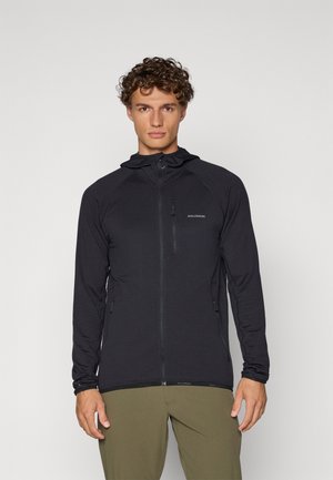 Veste légère noire avec fermeture éclair à l'avant, capuche et tissu texturé. Elle dispose de manches raglan et de deux poches latérales zippées.