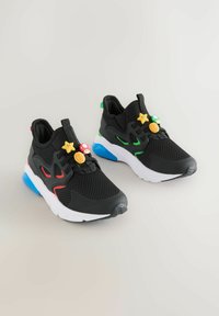 Black mesh sneakers with colorful plastic charms and contrasting sole accents, featuring red, green, and blue details for added visual interest.