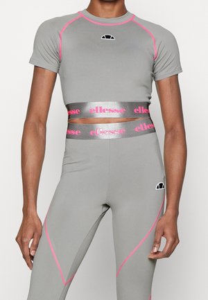 Person trägt ein eng anliegendes graues Crop-Top- und Leggings-Set mit pinkfarbenen Nahtakzenten und silbernen elastischen Bändern mit pinkfarbenen "ellesse" Logos rund um die Taille.