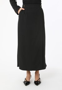 Jupe midi noire en tissu fluide et lisse, dotée de deux boutons à l'avant et de poches latérales. Ourlet cousu et coupe droite.