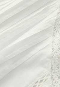 White fabric with vertical pleats, featuring intricate lace detailing on one edge. Smooth texture, lightweight and airy appearance.