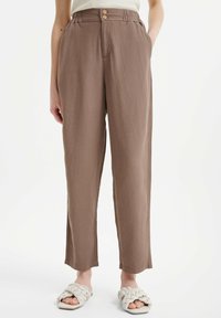 Pantalon marron clair à coupe décontractée avec une ceinture élastique et deux boutons en bois. Fabriqué en tissu doux avec une texture lisse.