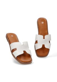 Chanclas blancas con un diseño de corte ancho, plantilla de cuero marrón y costuras en contraste. Suela plana, punta abierta y estilo sin talón.