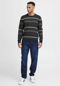 Kootud kampsun horisontaalsete triipudega tumesinises, beežis ja pruunis. Koos tumesiniste teksade ja valgete ketsidega mustade aktsentidega.