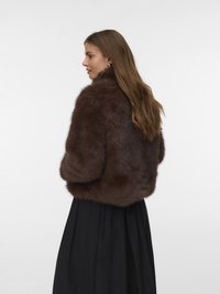 Brun pelsjakke med høj krave, blød tekstur og cropped design. Båret over en flydende sort nederdel med en fuld silhuet.