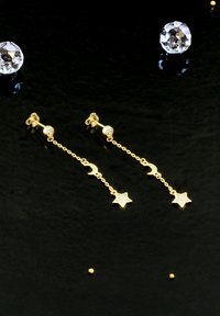 Guldörhängen med hängande månskära och stjärnpendlar, accentuerade med dekorativa stenar, mot en svart bakgrund.
