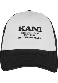 Čierna a biela trucker capka s zakriveným brímom; obsahuje "KANI THE ORIGINAL EST. 1989 REG. OBCHODNÁ ZNAČKA" v tučných čiernych písmenách.
