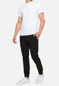 T-shirt blanc à manches courtes associé à un pantalon cargo noir et des baskets blanches. Le pantalon cargo comprend des poches latérales et une coupe fuselée.