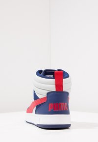 Vysoké tenisky v kombinaci modrých, bílých a červených materiálů, s polstrovaným límcem a výrazným červeným logem "PUMA" vzadu.