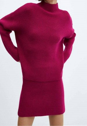 Femme portant un pull texturé magenta à manches longues et col montant avec une jupe magenta ajustée assortie.