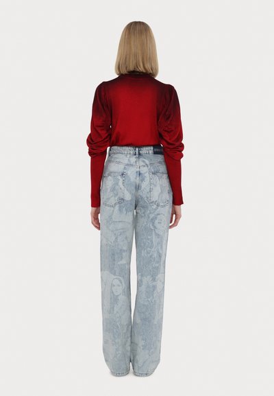 Červený dlouhý rukáv s nařasenými rukávy, kombinovaný se světle modrými kalhotami s širokými nohavicemi, které mají vybledlý grafický vzor. Zadní pohled, minimální detaily.