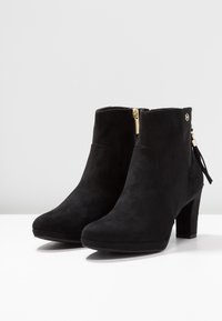 Černé semišové ankle boot s špičatou špičkou, 9 cm podpatkem, zlatým zipem a třásní na zadní straně. Hladká textura.