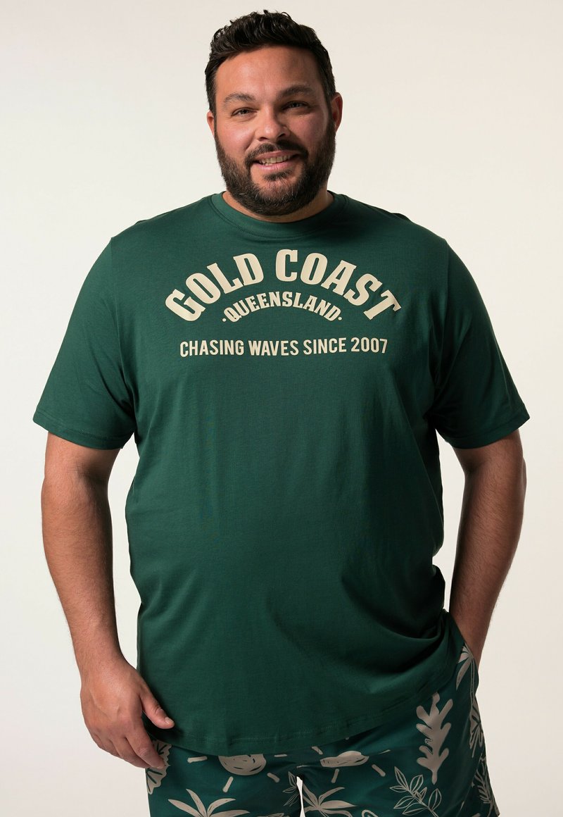 Zelené bavlněné tričko s potiskem "GOLD COAST, QUEENSLAND" a "CHASING WAVES SINCE 2007" v béžové barvě. Krátké rukávy a kulatý výstřih.