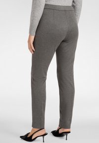 Szare, dopasowane spodnie o gładkiej teksturze, z talią na średnim poziomie i zwężanymi nogawkami, w połączeniu z czarnymi butami na obcasie typu slingback.