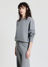 Felpa grigia con una trama morbida, caratterizzata da un collo rotondo e una vestibilità rilassata. Abbinata a pantaloni grigi con coulisse per un look coordinato.