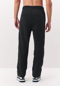 Black sweatpants with an elastic waistband, two back pockets, and a relaxed fit. Features cuffed bottoms and a smooth texture.