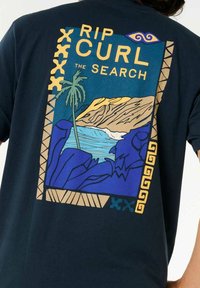 Marineblå t-shirt med et farverigt grafisk motiv af en strandscene med palmetræer, bjerge og hav, omkranset af dekorative mønstre.